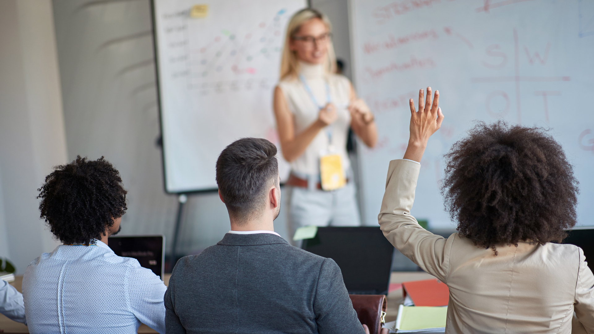 Blonde female professor teaching three students with black female student's hand raised